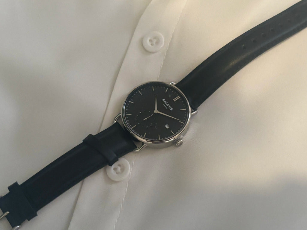 Montre éco-responsable Baldus Paris en acier recyclé avec bracelet en cuir noir, posée sur une surface blanche